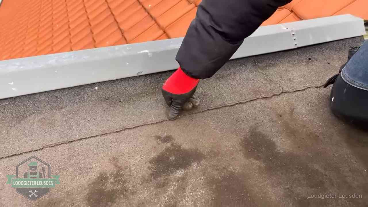 Vakman wijst een naad met vochtplekken aan op een bitumen plat dak in Leusden