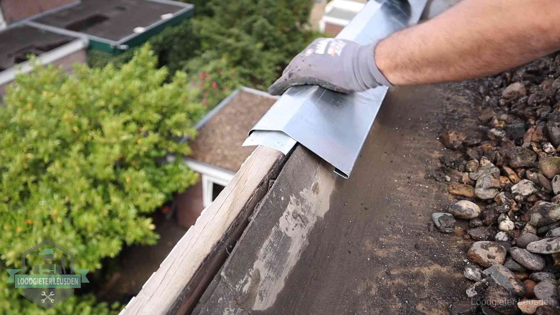 Dakdekker plaatst een zinken deklijst op een dakrand met uitzicht over een woonwijk in Leusden