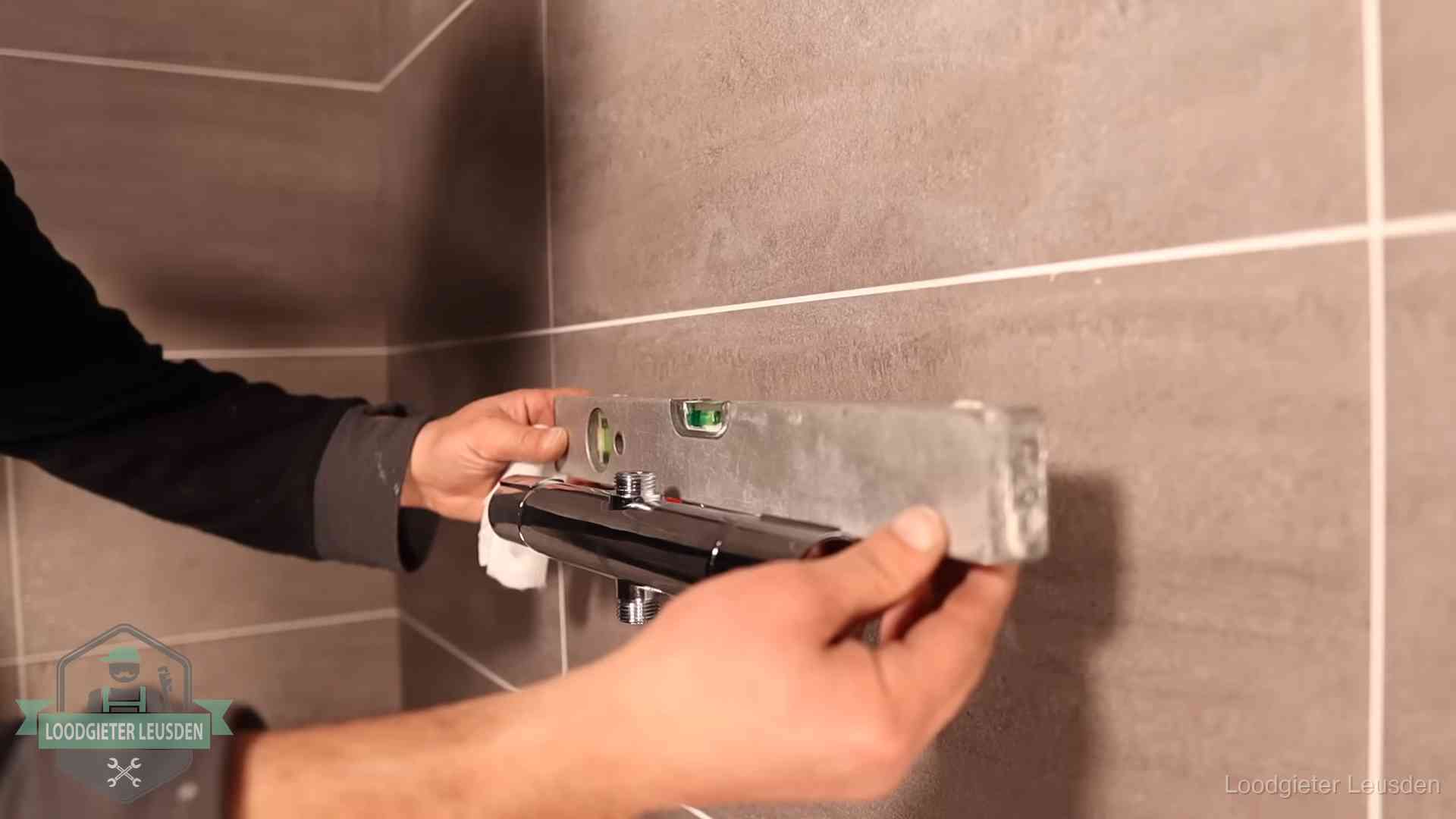 Loodgieter lijnt een douchekraan uit met een waterpas in een woning in Leusden