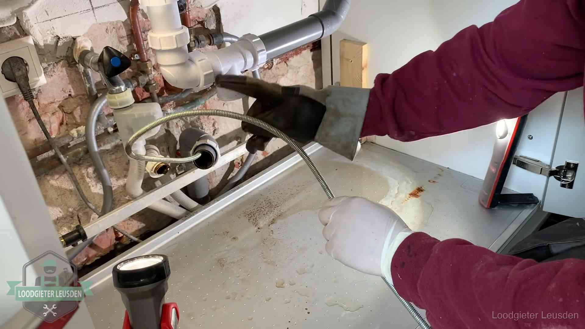 Ontstoppingsveer gaat in een geopende sifonaansluiting onder het aanrecht in Leusden