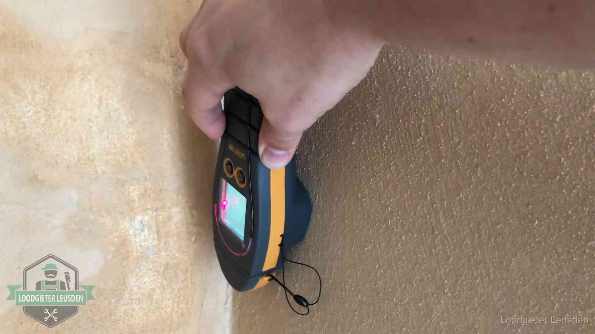 Vochtmeter tegen een muur met vochtplekken tijdens het opsporen van een daklekkage in Leusden
