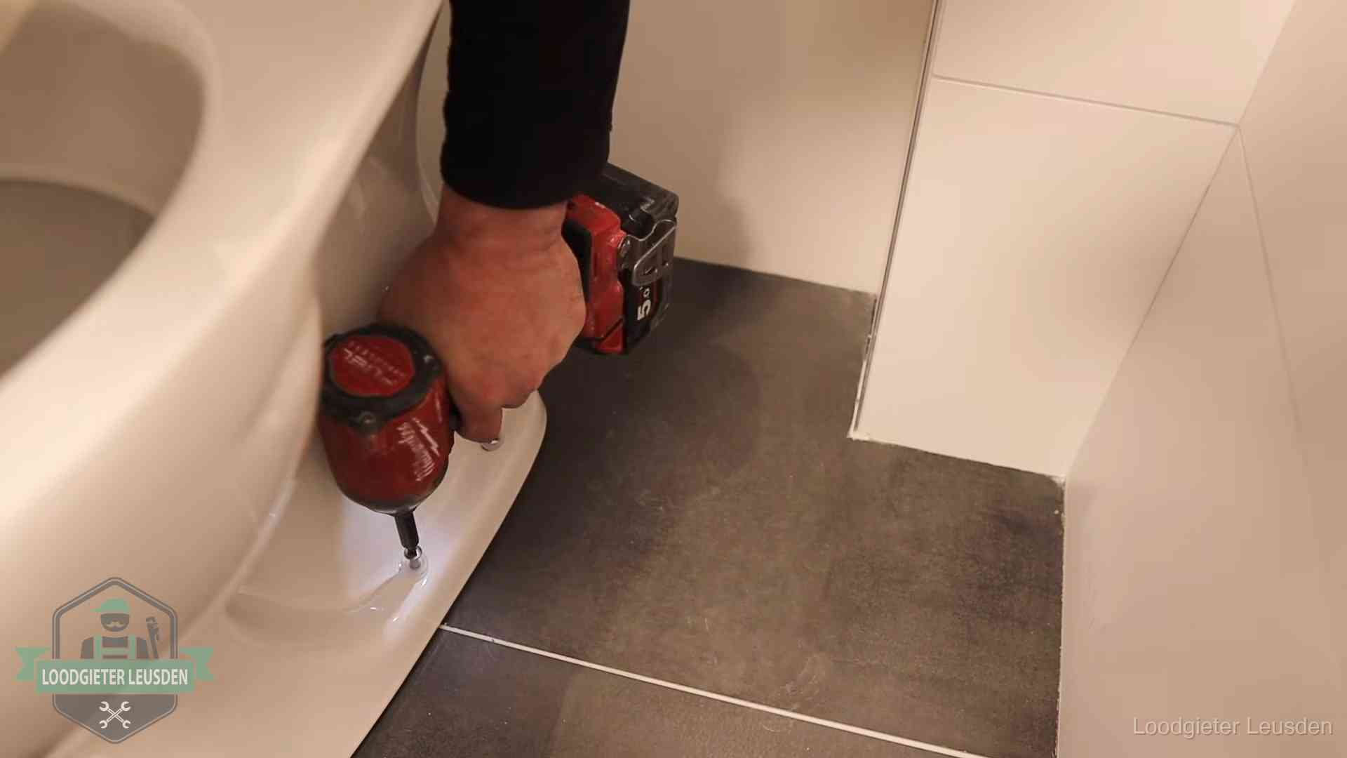 Loodgieter zet de voet van een wc-pot vast op de tegelvloer in Leusden